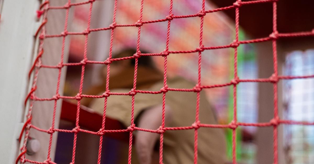 A child climbs on a play structure in the background of a red safety net.