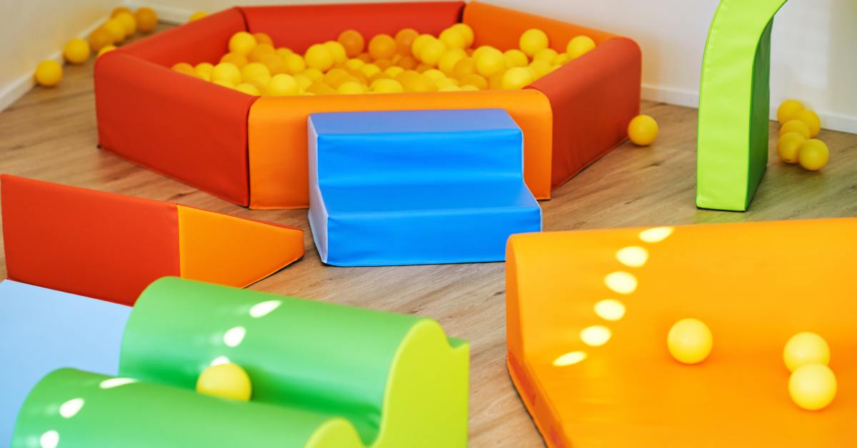 A variety of colorful soft-play structures, including a small, hexagonal ball pit, fill an indoor play center.
