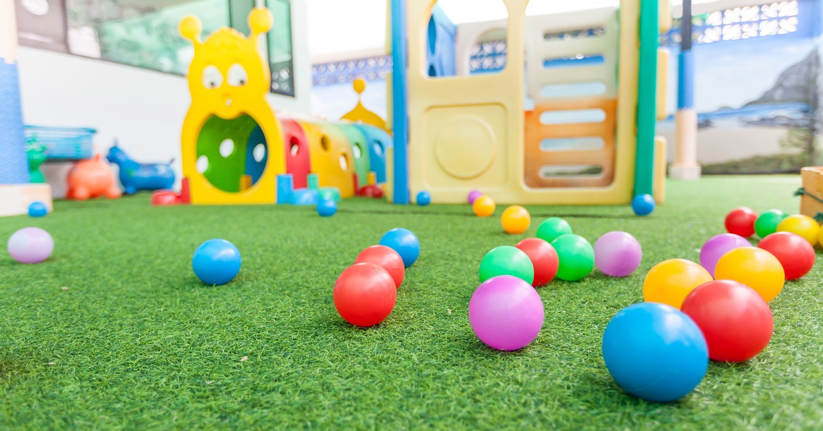 Plastic play structures in an indoor playground with green faux grass and several colorful play balls in the foreground.