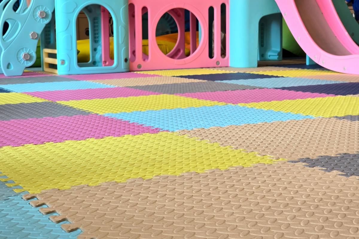 Colorful foam puzzle mat flooring in an indoor playground, with a plastic pink and blue play structure in the background.